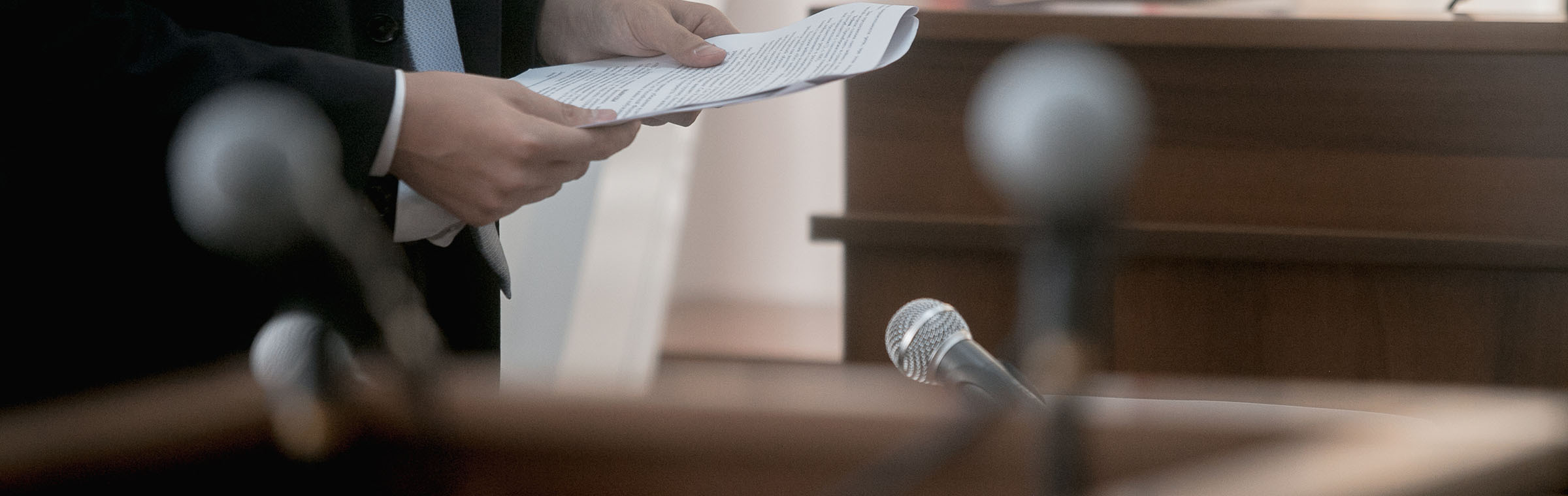 close up of microphones in a court room with a man holding papers in the background