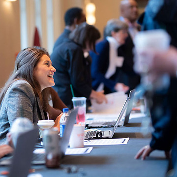 young professional woman smiling while helping seminar attendees at a check in table