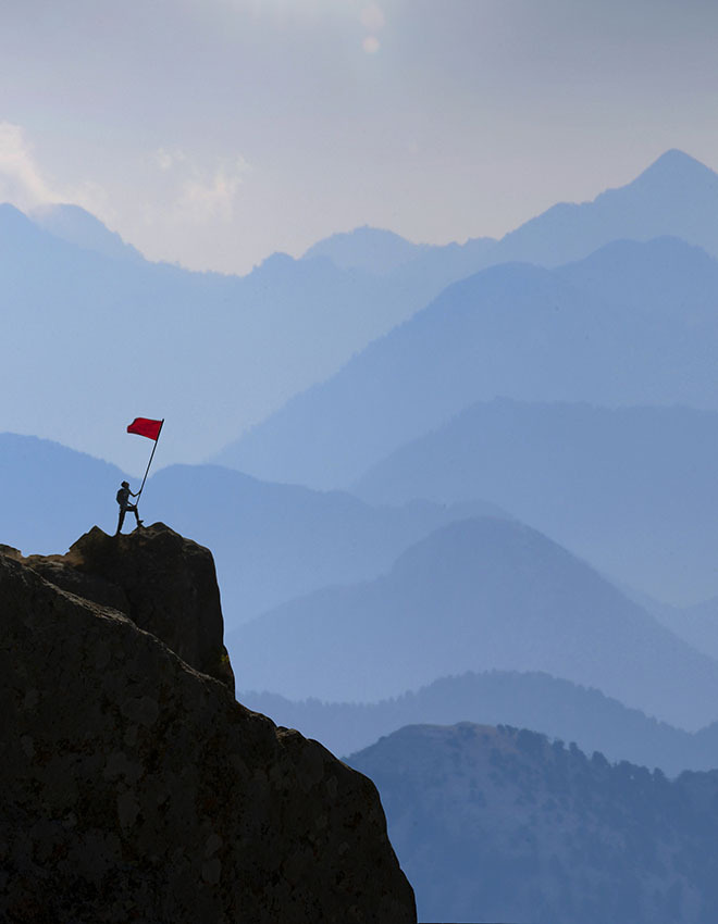 silhouetted person planting a red flag on a mountain ledge