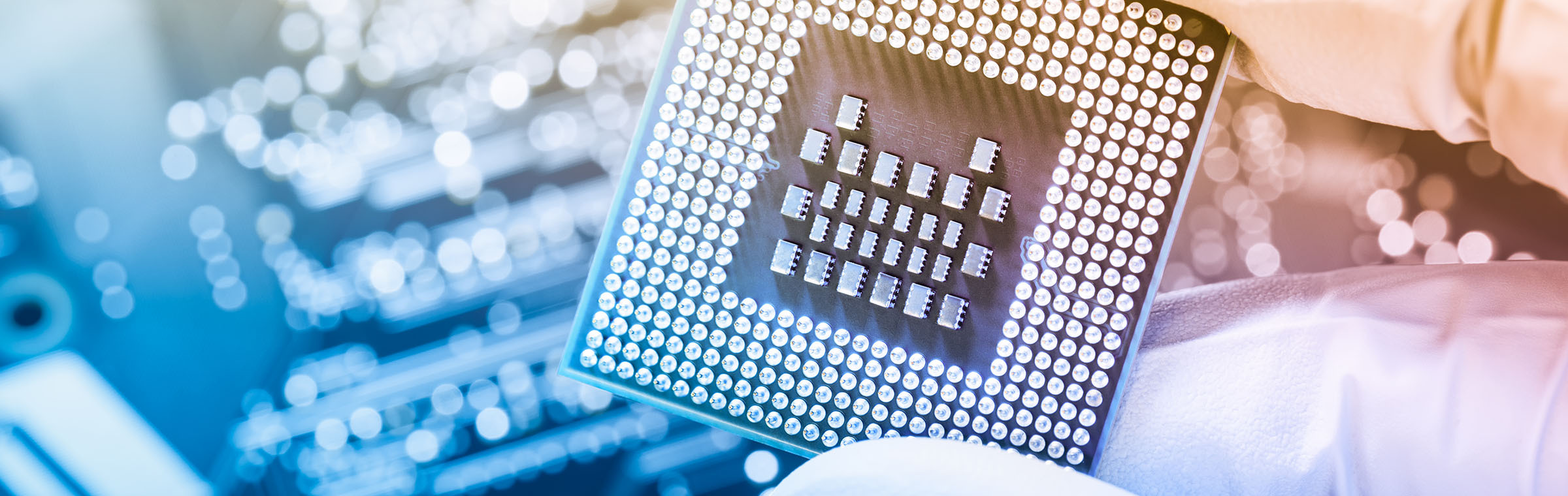 gloved hand holding microchip with circuit board in background