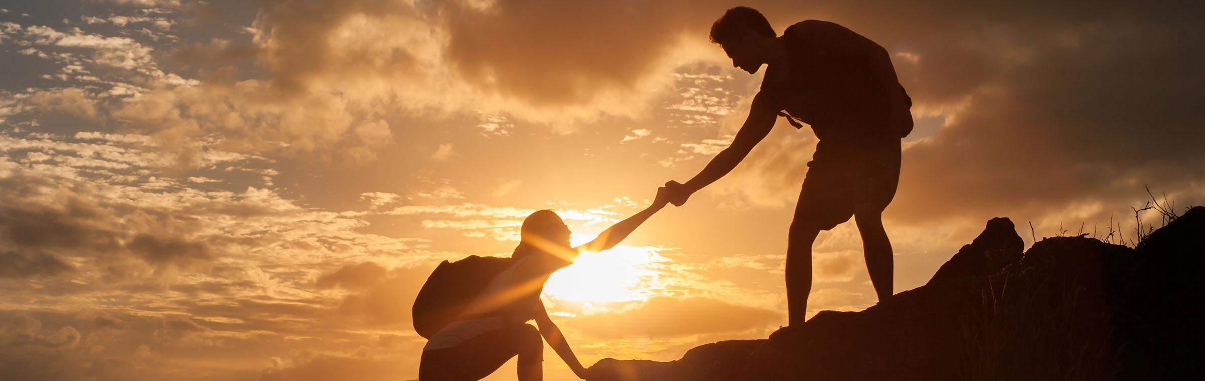 in silhouette; hiker helping another hiker climb a rock