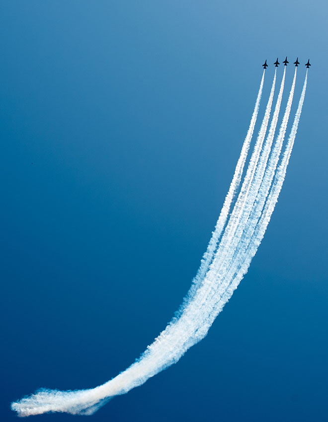 five jets flying upwards in formation against a blue sky