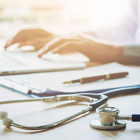 Doctor typing information on laptop in hospital office, focus on stethoscope