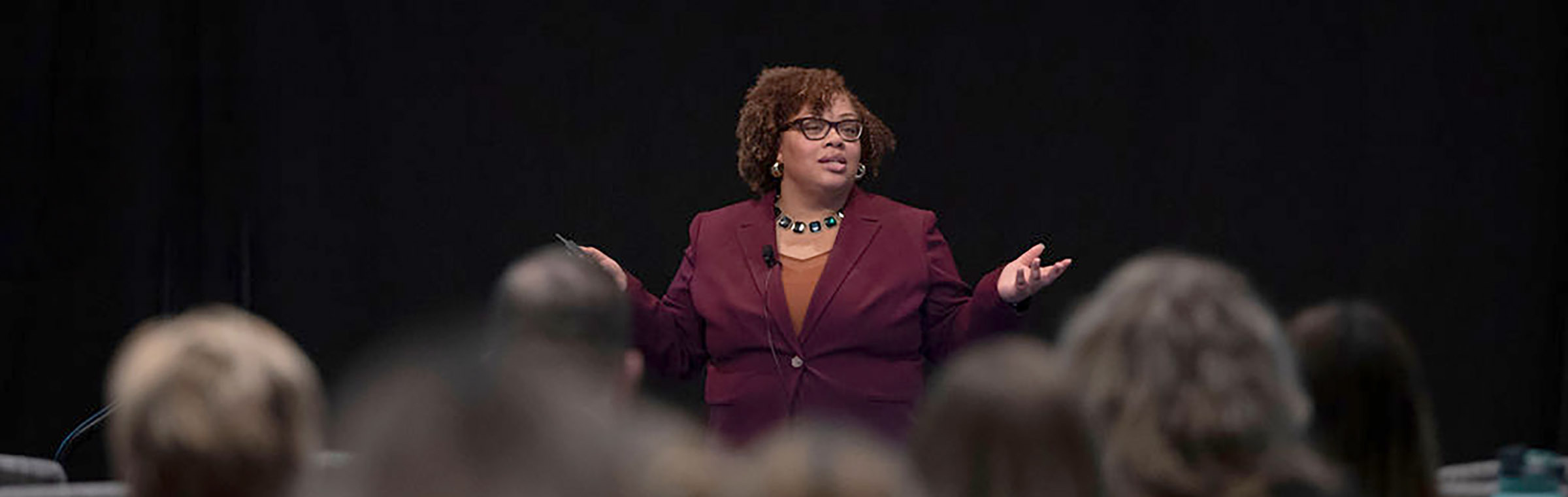 Patice Holland speaking before a crowd, dark background