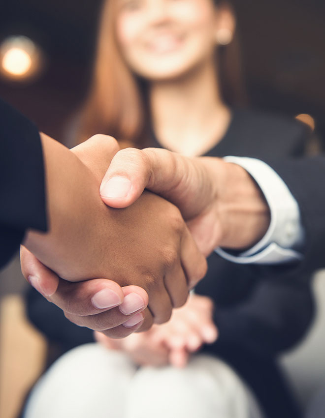 closeup of a handshake with a young woman in the distance